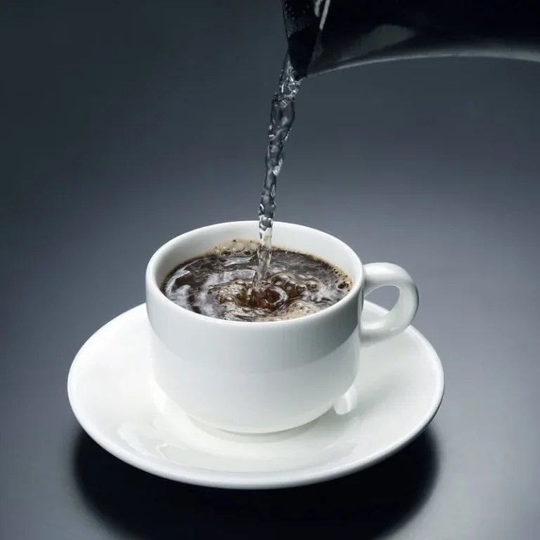 Przegotowaną wodę wlewa się do białego kubka z czarną kawą