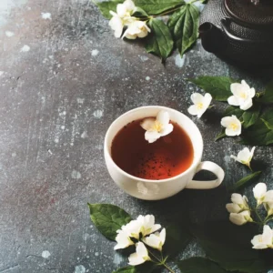 Tło jaśminu herbaty z czajniczkiem, liśćmi i kwiatami na ciemnej teksturze, widok z góry