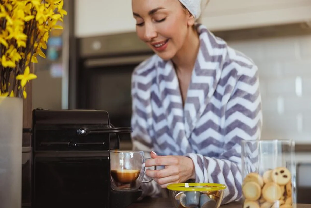 Kobieta robi filiżankę kawy z ekspresu w kuchni