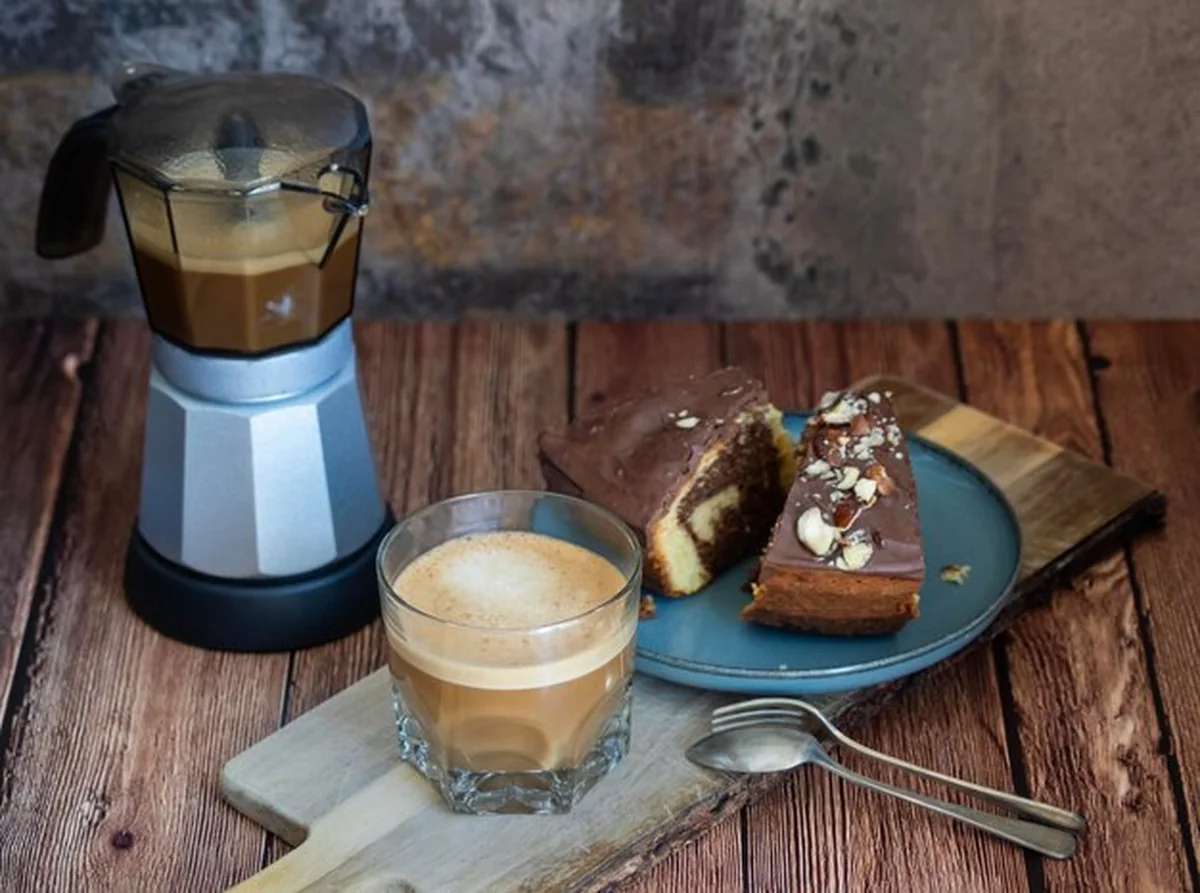 Szklanka kawy z mlekiem obok automatu do kawy i ciasta