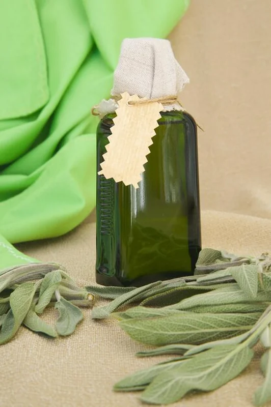 Butelka olejku z szałwii. Świeże liście szałwii w tle