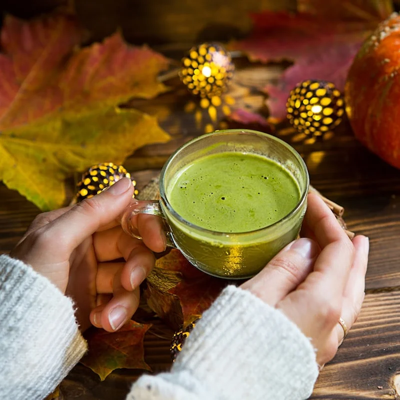 Drewniany stół z matchą i kobiecą dłonią w swetrze na pucharze