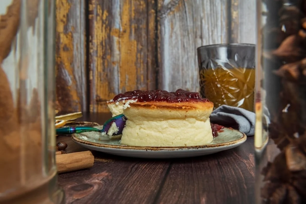 Sernik z dżemem jagodowym obok szklanki soku między drewnianymi ścianami