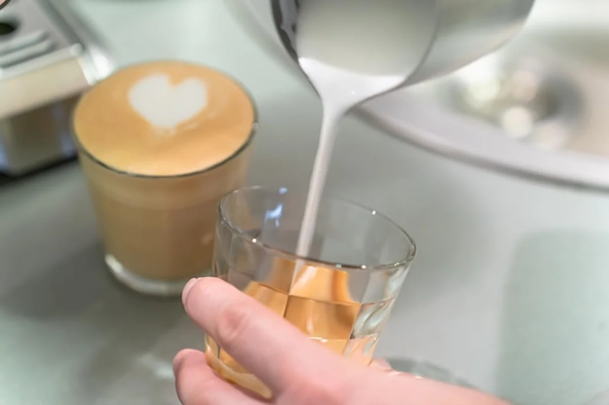 Barista wlewa mleko do szklanki z kawą