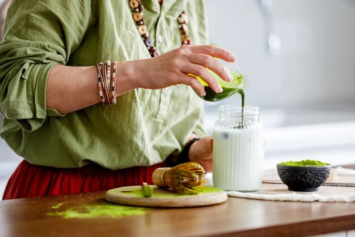 Kobieta przygotowująca herbatę matcha dodająca herbatę do mleka na matcha latte z bliska