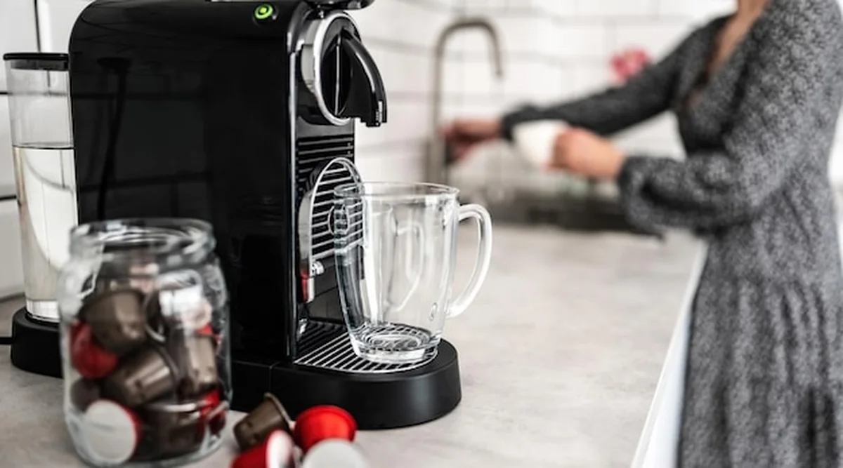 Maszyna do kawy z kapsułkami i przezroczystym kubkiem w kuchni domowej