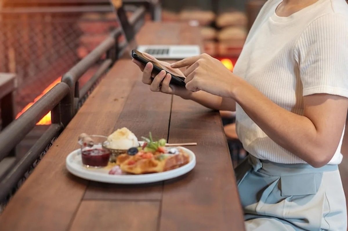 Kobieta używająca smartfona jedząca deser ze świeżymi jagodami i owocami w kawiarni