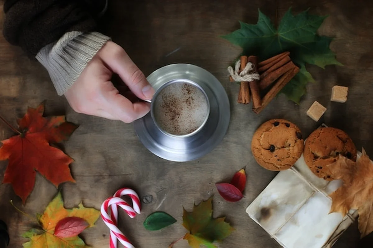 Ręce trzymające kubek gorącej kawy na stole z liśćmi